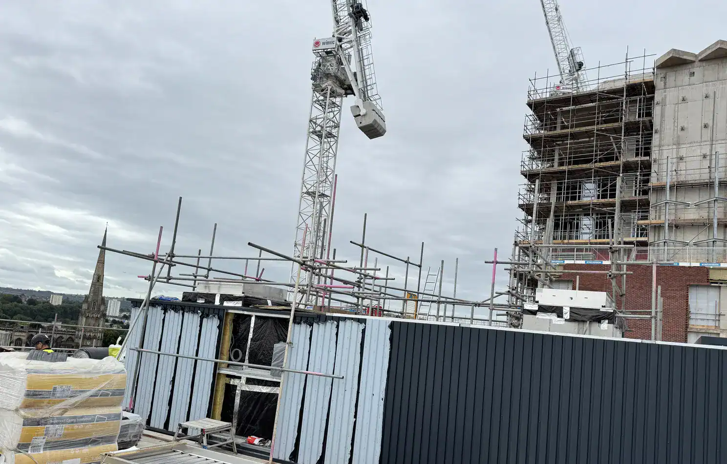Facade installation area with scaffold access and tower cranes on a live construction site.